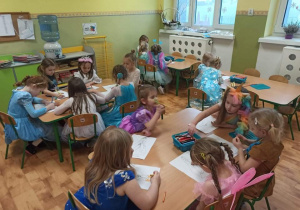 Dzieci w karnawałowych strojach siedzą przy stolikach i kolorują obrazki.